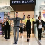 The picture shows a group of models/dancers performing a pop up fashion show directly outside a retails store in a shopping mall.