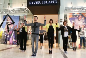 The picture shows a group of models/dancers performing a pop up fashion show directly outside a retails store in a shopping mall.