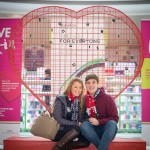 Couple sitting below giant Valentine heart installation filled with padlocks at Love Lock-In retail event, Cardiff