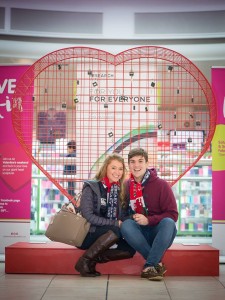 Couple sitting below giant Valentine heart installation filled with padlocks at Love Lock-In retail event, Cardiff