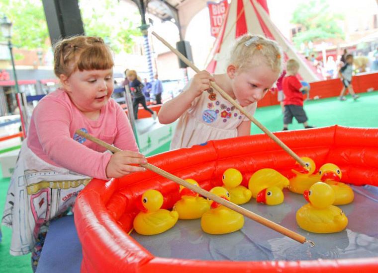 Two young girls play hook-a-duck at a carnival event