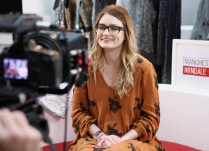 View from behind the camera of a young woman is being filmed as she records a video blog, live on a shopping mall.