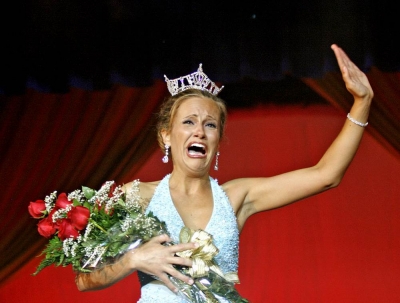 Portrait of female beauty pageant winner accepting her award. She is waving and crying with happiness, clutching a bouquet of roses and wearing a diamond tiara.