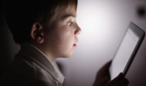 Experiential learning. Little boy sat in dark room looking at tablet. The light from the screen illuminates his face.