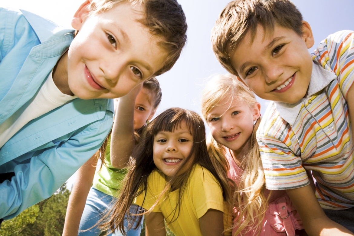 Close up photo of a group of friends, kids age 6-10, looking towards camera and smiling.