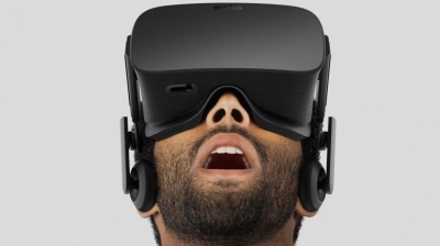 A man, wearing Virtual Reality googles, is looking upwards. His mouth is open in an expression of complete wonder.